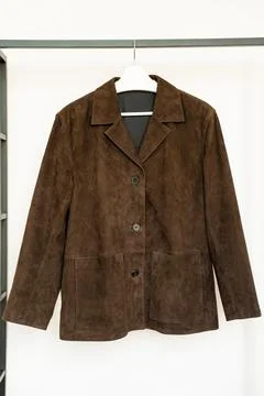 Dark brown suede jacket with buttons and patch pockets hanging on white hanger Stock Photos