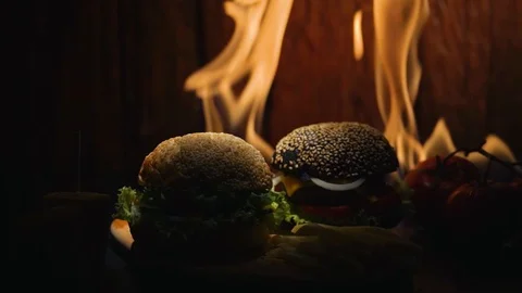 A dark bun burger, tomatoes, corn and a fry potato are lying on a wooden table Stock Footage 115761022