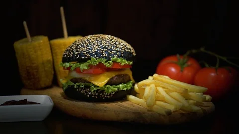 Dark bun burger, tomatoes, corn and french fries lie on a wooden table on a Stock Footage 115761254
