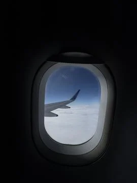 Dark cabin airplane window framing wing and cloud layer creating serene bus.. Stock Photos