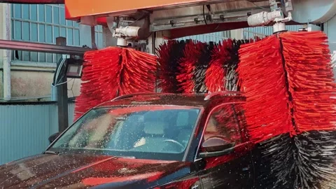 Dark car covered in soap moving through automatic wash tunnel with red and black Stock Footage 330740938