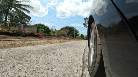 Dark car travels down paved road past buildings and palm trees Stock Footage 307484411