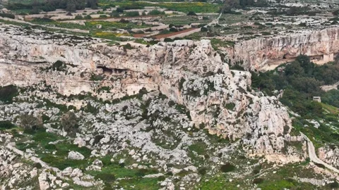Dark cave openings pock the limestone walls of a malta valley patchwork farmland Stock Footage 343580584