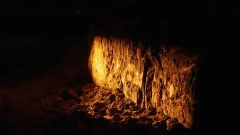Dark cave wall with textured rock illuminated by warm light Stock Photos