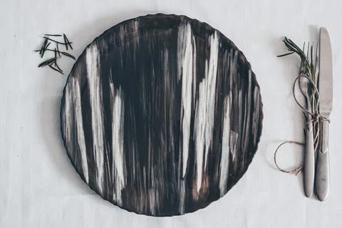 Dark ceramic plate with marble texture on white linen table setting with Stock Photos