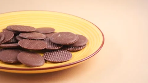 Dark chocolate coin chips rotating on yellow ceramic plate against beige ba.. Stock Footage 331996772