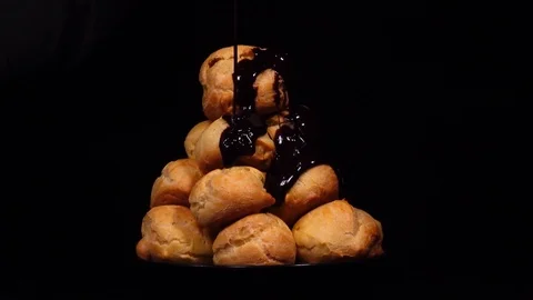 Dark chocolate pouring of ruddy eclairs in pyramid, rotating on black background Stock Footage 74929983