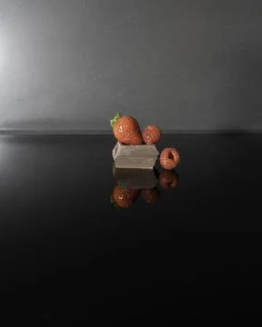Dark chocolate, strawberry and raspberry on black surface with reflection Stock Photos