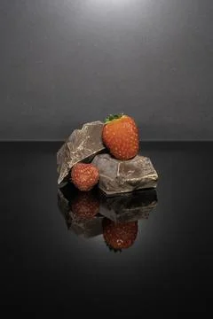 Dark chocolate, strawberry and raspberry on black surface with reflection Stock Photos