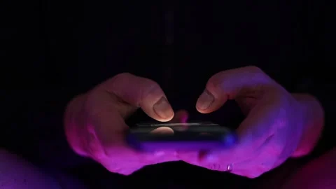 Dark Close-up of hands using a mobile phone scrolling with screen reflections Vidéo 336811661