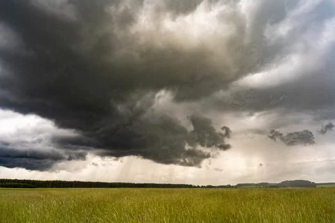 A dark cloud hangs low over the green field, and it is raining in the distance Foto stock