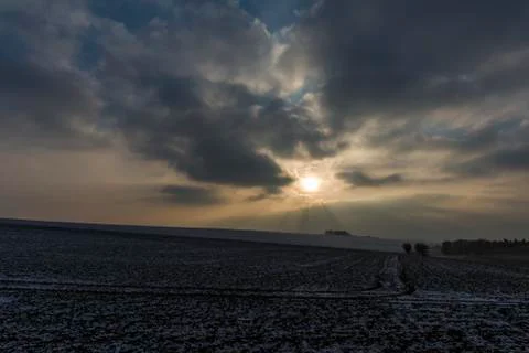 Dark clouds and sun over frozen field Stock Photos
