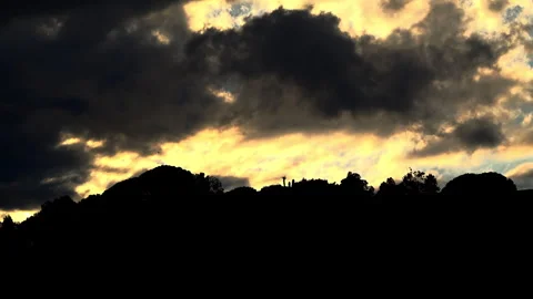 Dark clouds drift over a glowing yellow sky above a hilltop Stock Footage 315249644