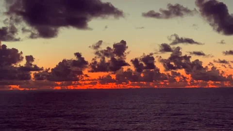 Dark clouds fill the sky above a calm ocean during a vibrant orange sunset Stock Footage 338282791