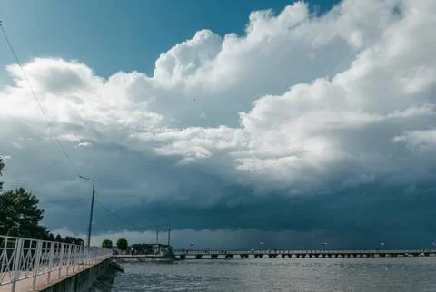 Dark clouds gather above the river, signaling an impending storm at dusk Stock Photos