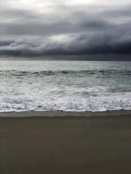Dark Clouds Gather Over Calm Waves at the Beach During Twilight Hours Stock Photos