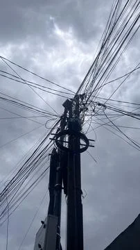Dark clouds loom behind a utility pole with numerous overhead wires and a cir Stock Photos