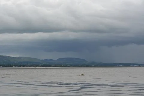 Dark Clouds Loom Over Tranquil Waters Near Quiet Hills in the Distance Stock Photos
