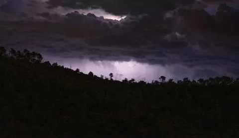 Dark clouds over a silhouette of trees at night, storm looming Stock Photos