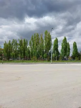 Dark clouds over the trees in spring time, Empty road foreground  Stock Photos