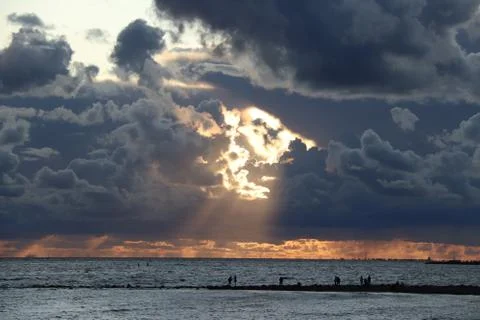 Dark clouds with rays in the center against the background of a sunset over the Stock Photos