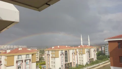 Dark clouds in sky cloudy. Tall buildings in distance. Big bright rainbow in sky Stock Footage 145769584