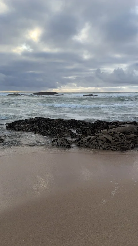 Dark clouds in sky as waves wash over rocky beach in Portugal. Panning shot. Stock Footage 237753702