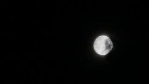 Dark clouds slowly moving through the full moon, shining on a black sky Stock Footage 98247088