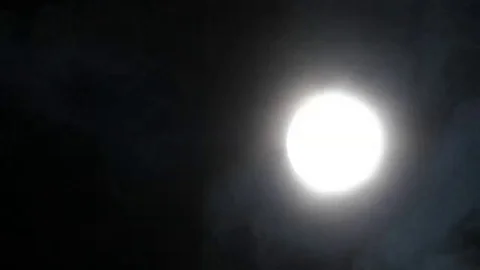Dark clouds slowly moving through the full moon, shining on a black sky Stock Footage 98247091