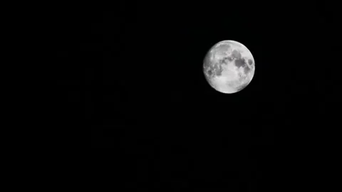 Dark clouds slowly moving through the full moon, shining on a black sky Stock Footage 98247092