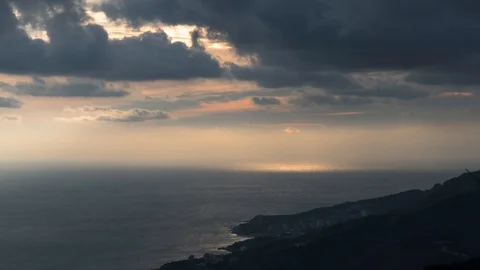 Dark clouds with sunbeams over sea near rocky coasts at sunset , time lapse Video stock 125451477