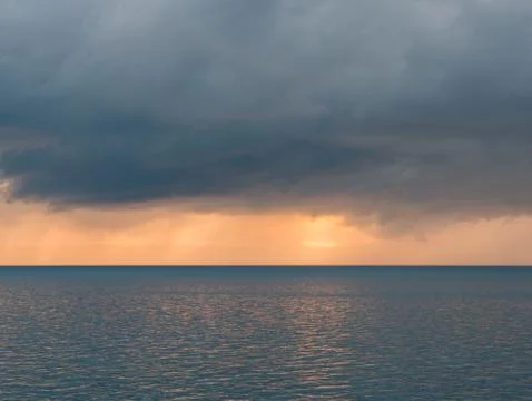 Dark clouds with sunlight over calm sea at sunset 库存照片