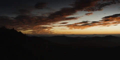 Dark clouds in the sunset sky over the silhouetted mountain ranges Stock Footage 103397481