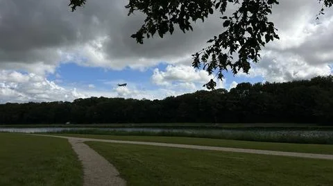 Dark cloudscape over riverside park with footpath and tree line, late-summer Stock-Fotos