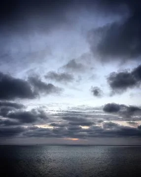 Dark cloudy sky over calm ocean water during sunset Stock Photos