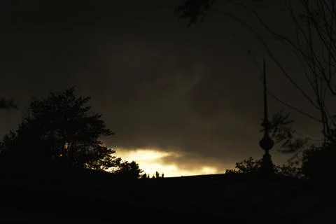 Dark cloudy sky with silhouettes of trees at sunset Stock Photos