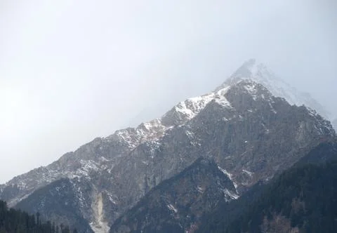 Dark cloudy Sky with snow-covered mountains and tall trees in Himachal Prades Stock Photos