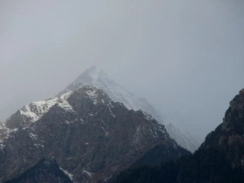 Dark cloudy Sky with snow-covered mountains and tall trees in Himachal Prades Stock Photos