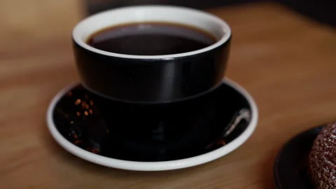 Dark coffee in black cup with matching saucer on wooden table, close view with Stock Footage 345373442