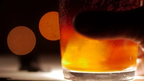 Dark colored cocktail with ice. Closeup shot on a blurry background. Hand Stock Footage 73997804