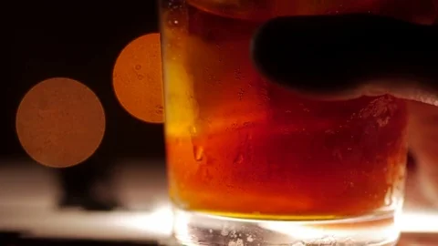 Dark colored cocktail with ice. Closeup shot on a blurry background. Hand Vídeo Stock 73997849