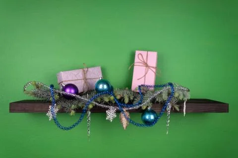 On a dark-colored shelf fixed on a green wall, coniferous branches are decora Stock Photos