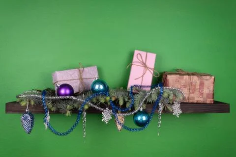 On a dark-colored shelf fixed on a green wall, coniferous branches are decora Stock Photos