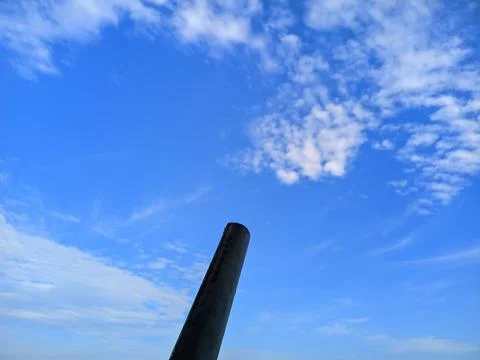 Dark Cylindrical Pipe Against Blue Sky with White Clouds 库存照片
