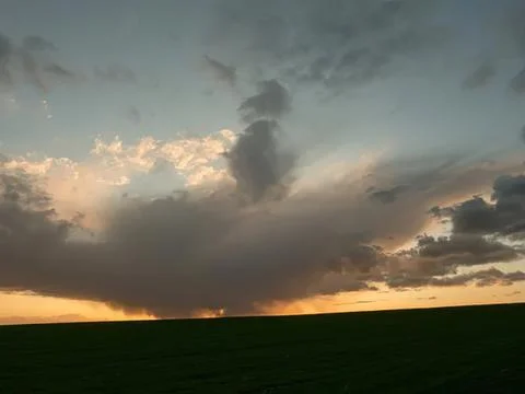 Dark dramatic clouds over a green field at sunset Stock Photos