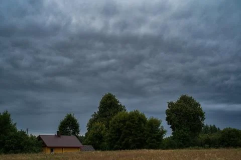 A dark, dramatic cloudy sky over a rural landscape with a small house 库存照片