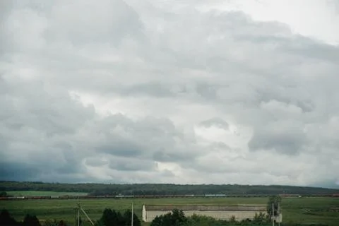 Dark dramatic rainy sky clouds over train composition in rural  farm landscape Stock Photos