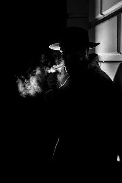 Dark dramatic silhouette of a man in a hat Smoking a cigarette on the street at Stock Photos