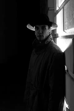 Dark dramatic silhouette of a man in a hat and raincoat at night on the street Stock Photos