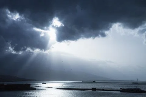 Dark dramatic sky with sunlight rays over sea Stock Photos